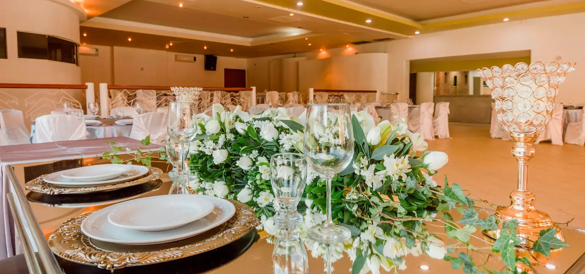 Mesa de banquete elegante con vajilla dorada, copas de cristal y arreglo floral blanco